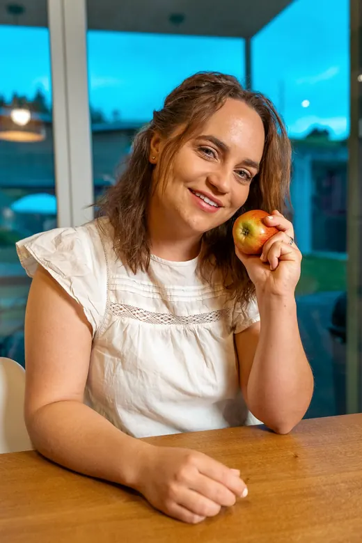 Norina sitzt am Küchentisch und lächelt, einen Apfel in der Hand