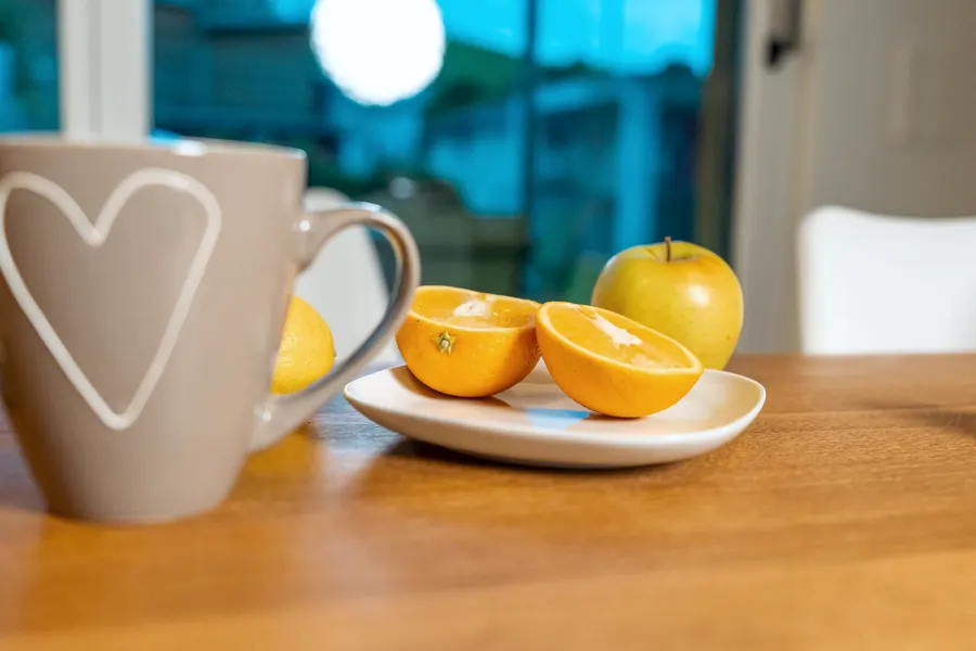 Tasse mit Herz, daneben halbierte Orange und Apfel auf einem Teller